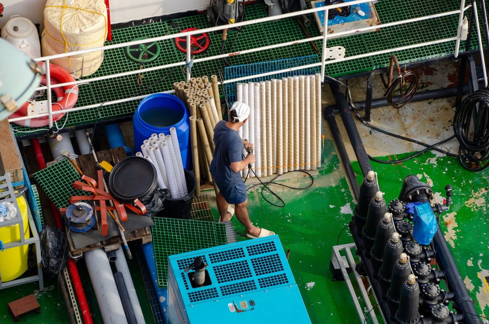 Worker handling coiled cable components on an equipment-filled ship deck