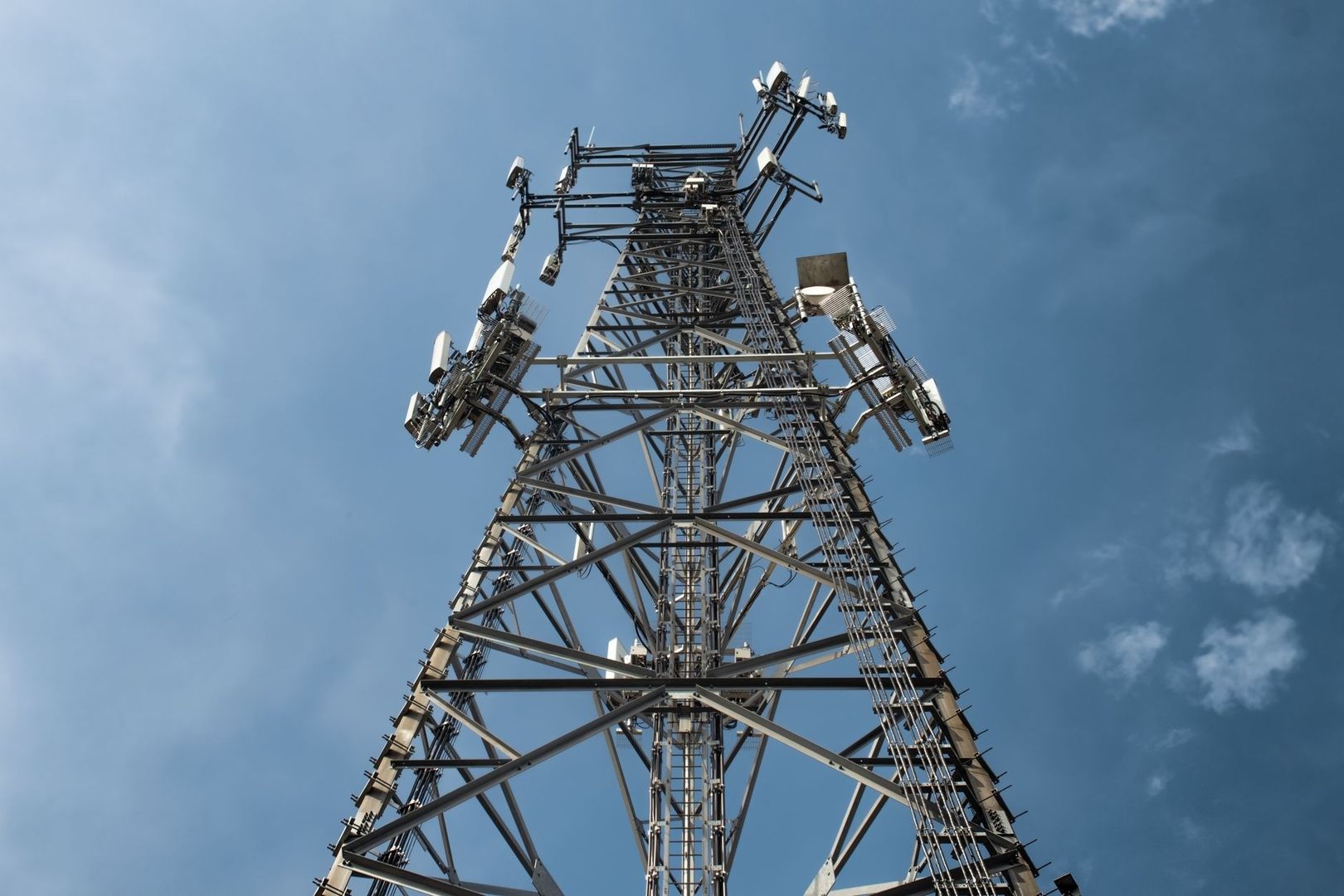 Low-angle view of a cellular antenna tower against a blue sky