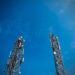 Two cellular communication towers with antennas against a blue sky