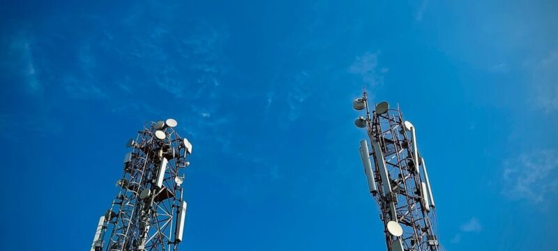 Two cellular communication towers with antennas against a blue sky